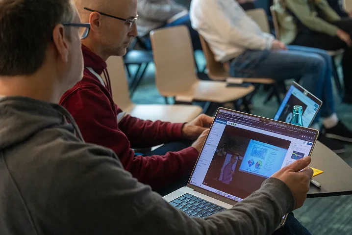 Teilnehmende schauen gemeinsam auf eine Session-Präsentation am Laptop bei einer früheren T4AT-Ausgabe
